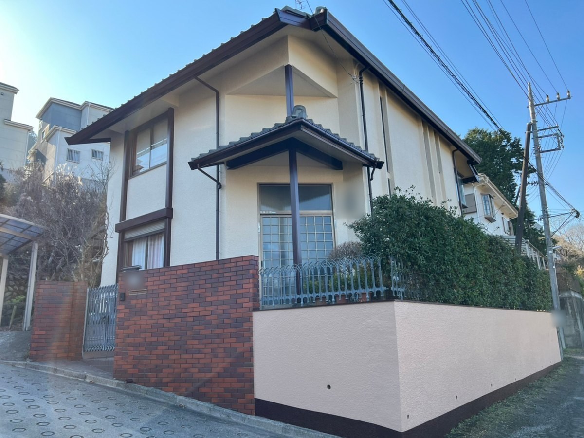 施工後の外観（道路の角から）。外壁は19-80D（クリーム色）、外構塀は15-60F（ピンクベージュ）